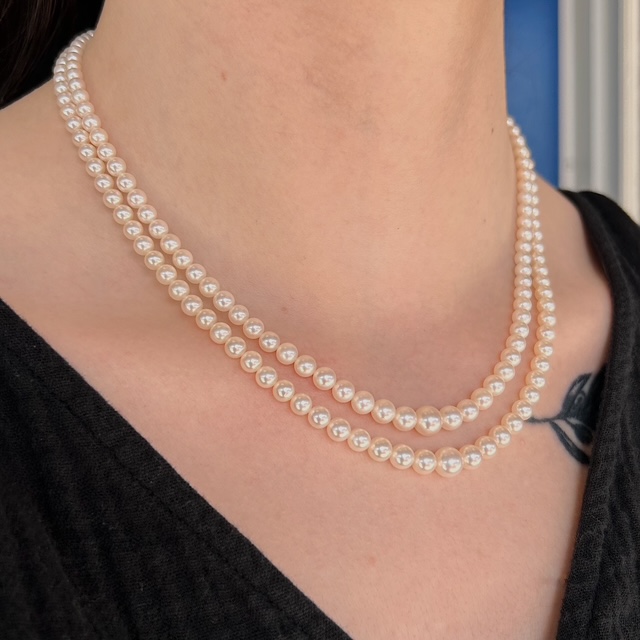 Two strands of white pearl necklaces draped around a person's neck against a black top.