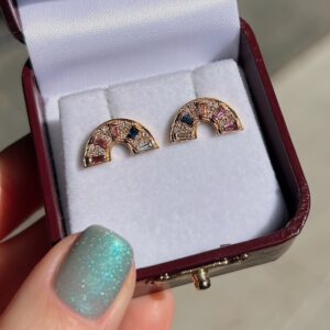 Pair of half-moon gemstone earrings in rose gold on white jewelry pad inside a maroon box.