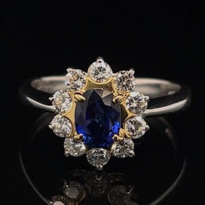 Ring featuring an oval deep-blue sapphire in a gold flower-shaped halo, encrusted with diamonds and set on a silver band.