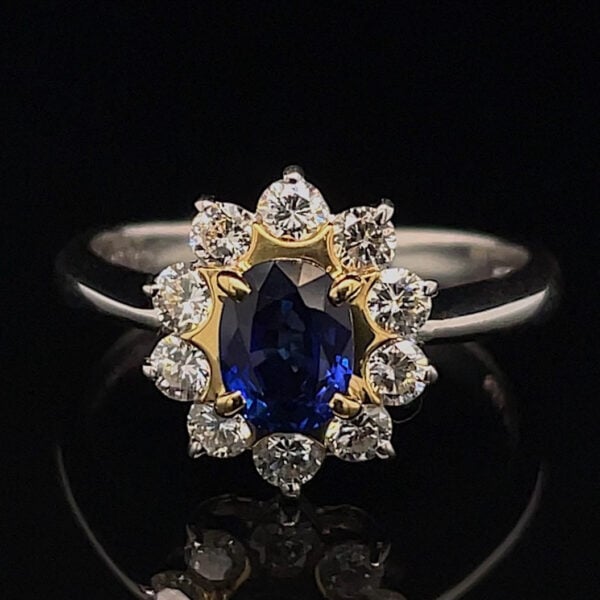 Ring featuring an oval deep-blue sapphire in a gold flower-shaped halo, encrusted with diamonds and set on a silver band.