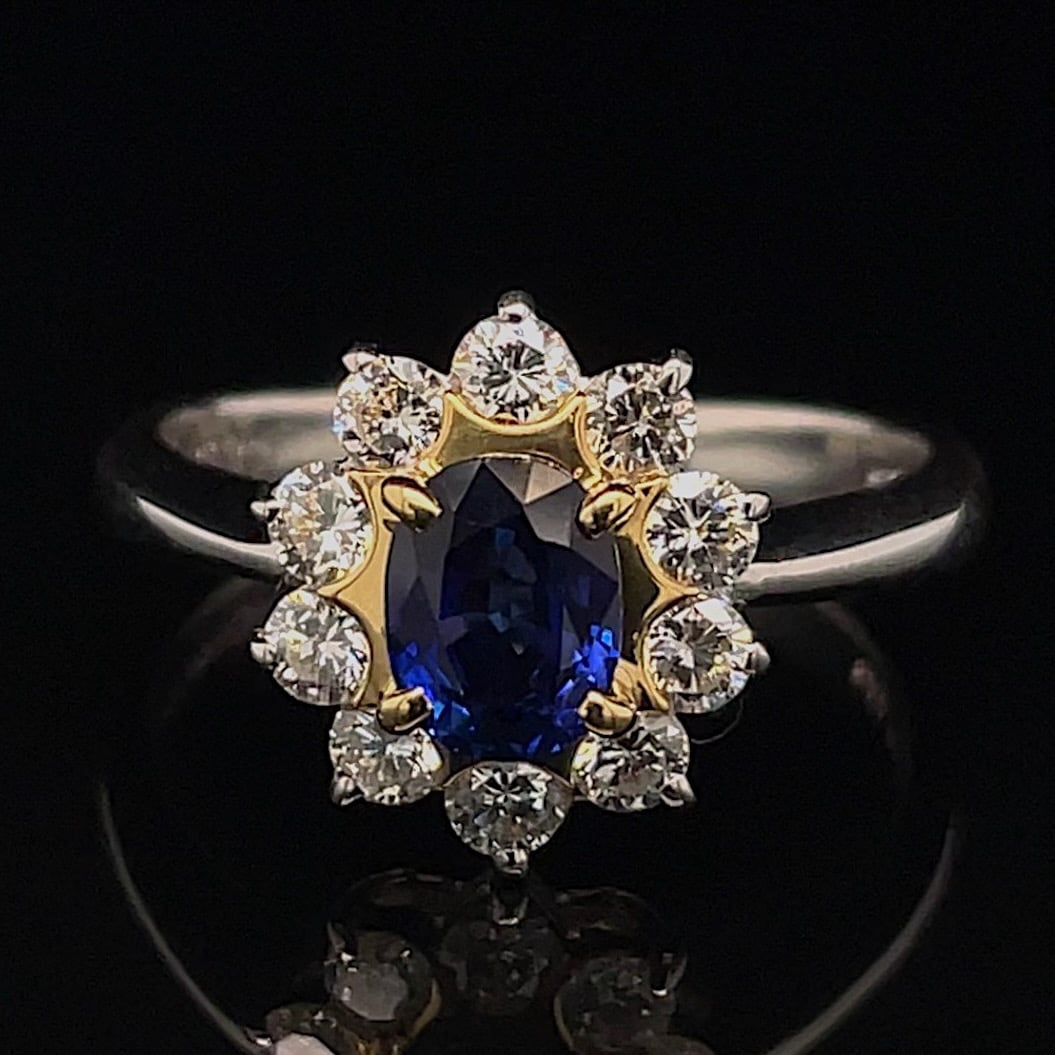 Ring featuring an oval deep-blue sapphire in a gold flower-shaped halo, encrusted with diamonds and set on a silver band.