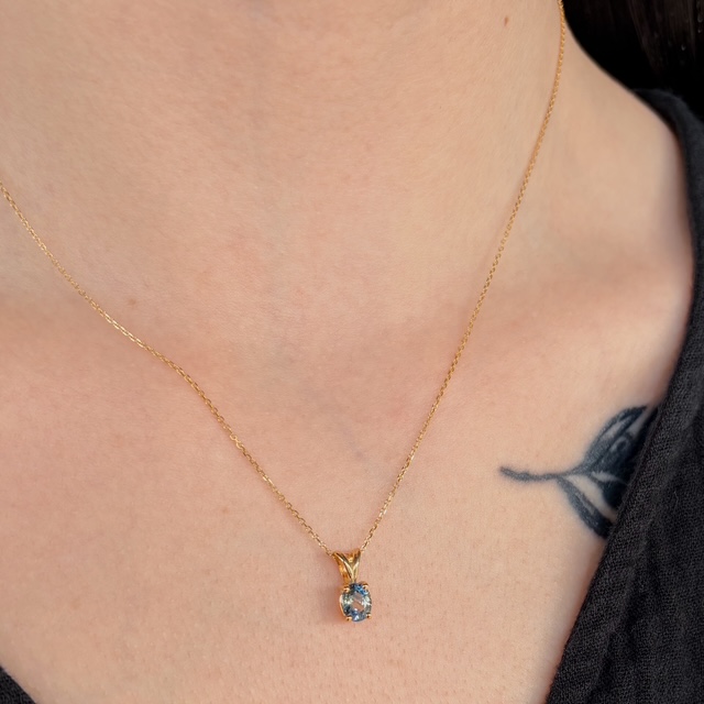 Gold chain necklace with a blue gemstone pendant resting on the collarbone
