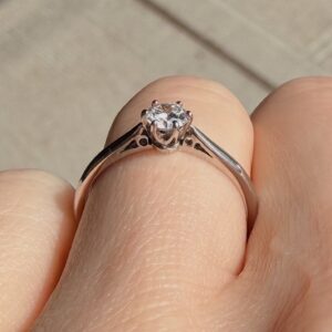 Close-up of a solitaire diamond engagement ring on a slender metal band with six prongs holding a bright diamond.