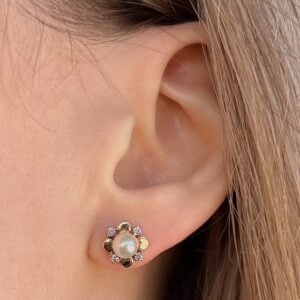 Close-up of a woman's ear wearing a gold-tone flower-shaped earring with a central pearl and tiny surrounding stones