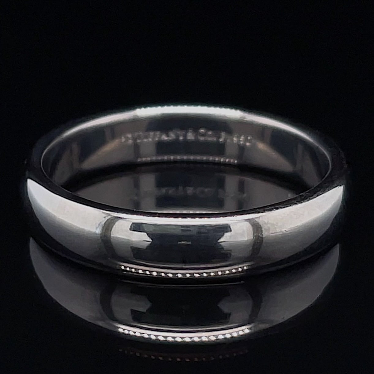 Shiny silver ring with a row of small diamonds along the outer edge, photographed on a dark background.