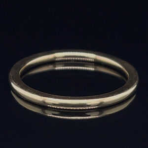 Silver wedding band on a dark reflective surface.