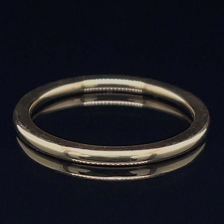 Silver wedding band on a dark reflective surface.