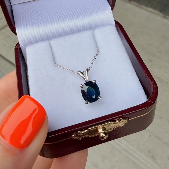 Silver necklace with an oval deep-blue gemstone pendant in an open jewelry box and white padding inside