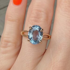 Oval blue gemstone ring on a finger with a rose-gold band and four prongs.