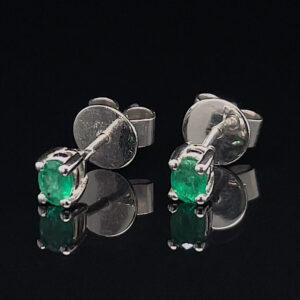 Emerald stud earrings with silver prong settings on a reflective black surface.