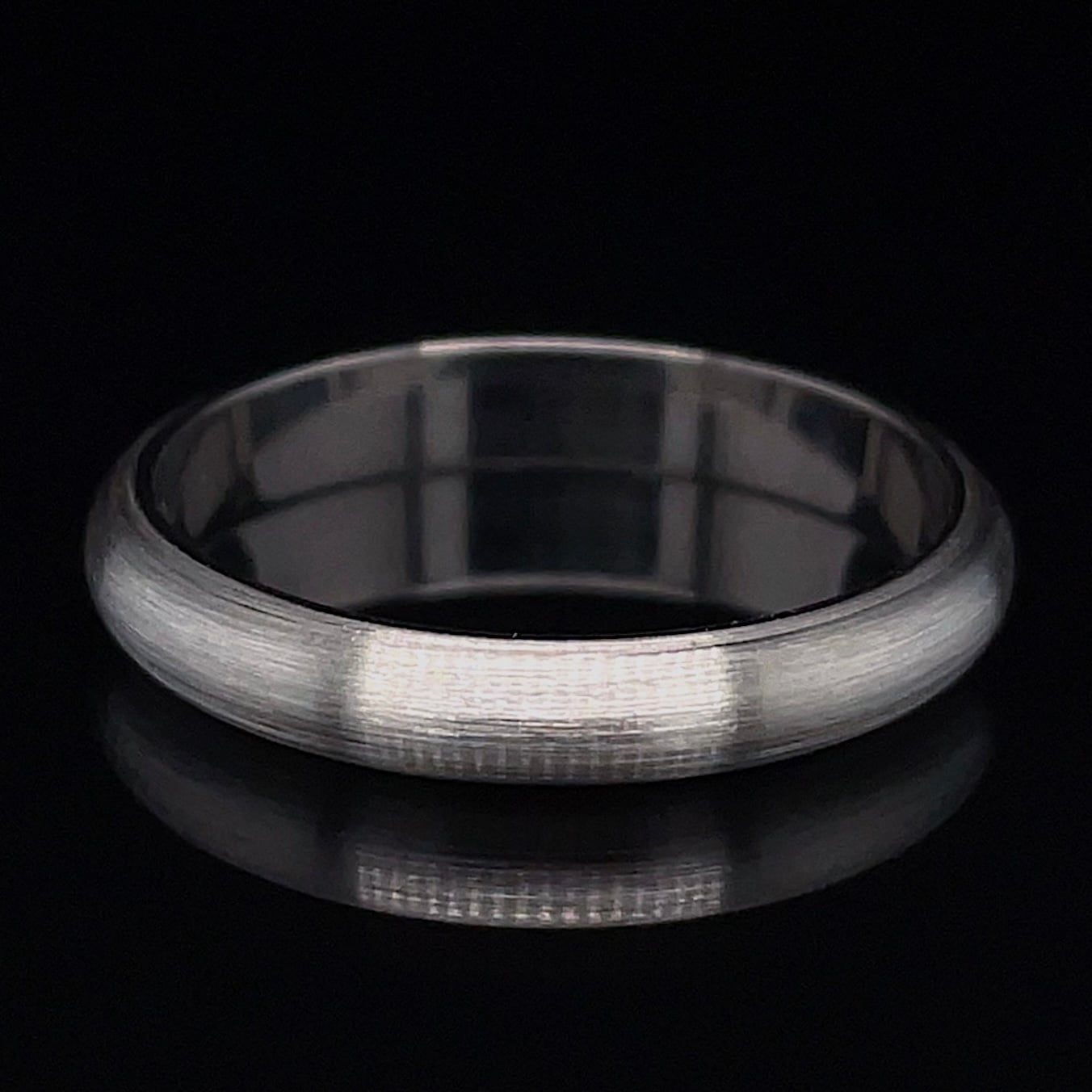 Brushed silver wedding band resting on a black background.