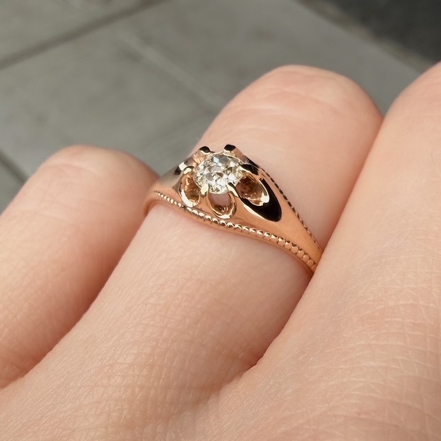 Rose gold engagement ring with a round diamond on a finger.