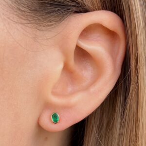 Green oval gemstone stud earring in the earlobe of a person, side view.