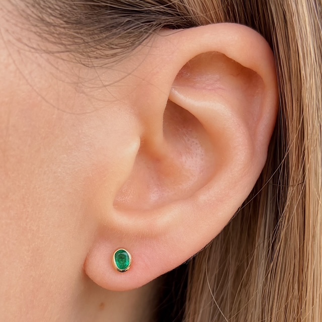 Green oval gemstone stud earring in the earlobe of a person, side view.