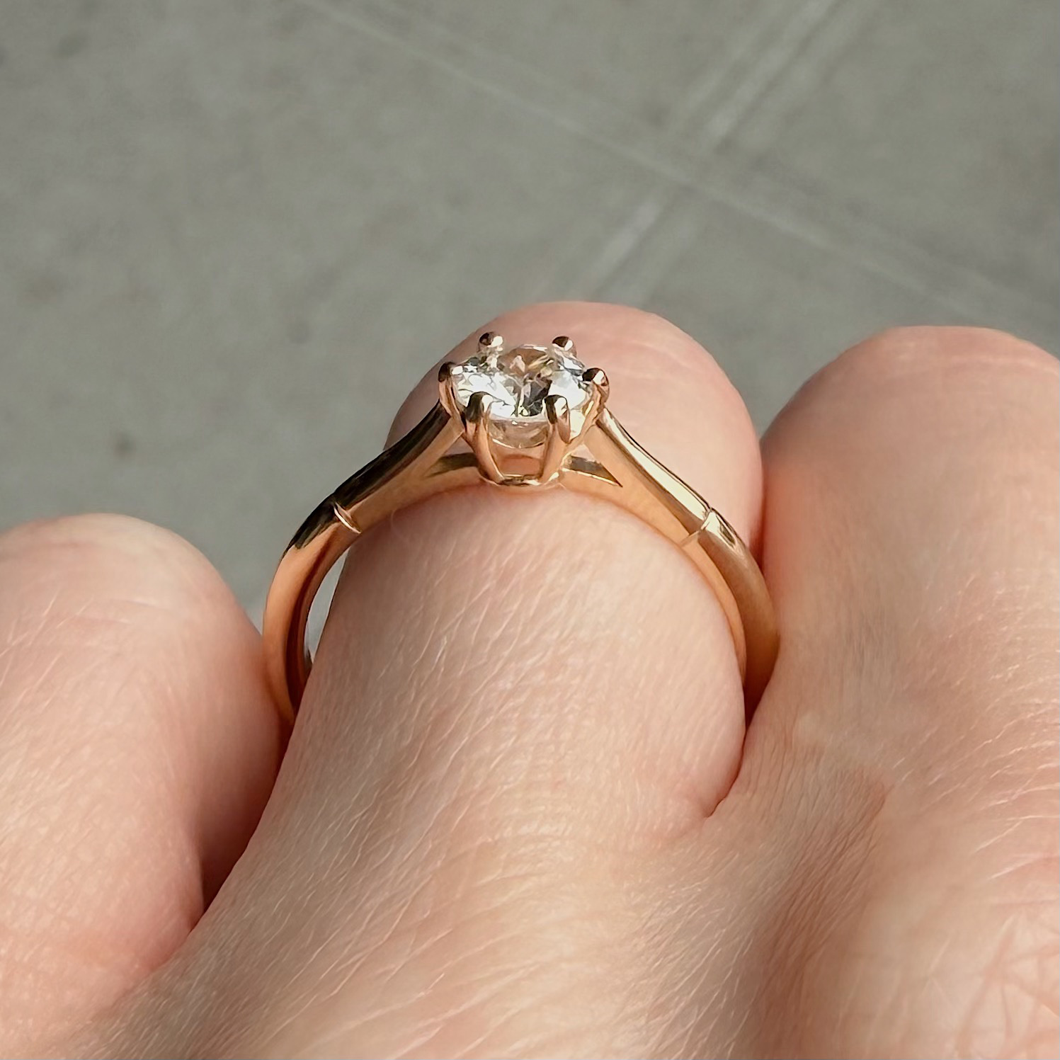 Rose-gold solitaire engagement ring with a round diamond held between two fingers.
