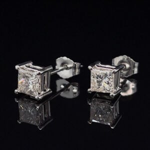 Pair of square princess-cut diamond stud earrings in a four-prong platinum setting on a black reflective surface