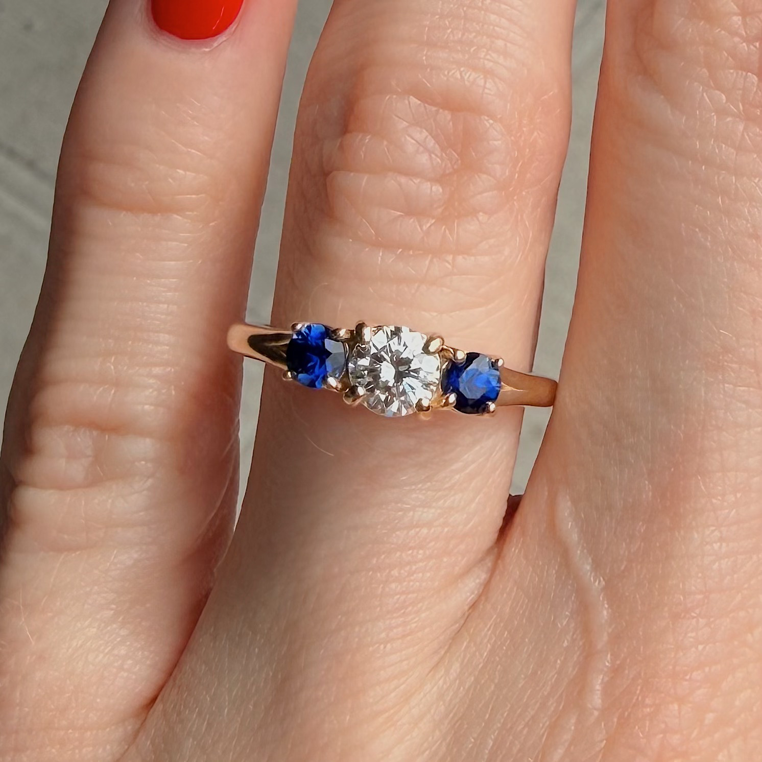 Rose gold ring with a central diamond flanked by two blue sapphires on the ring finger