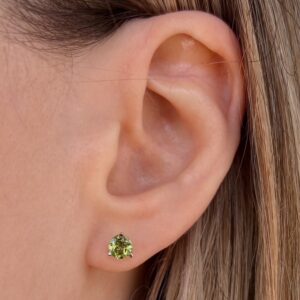 Close-up of a woman's ear wearing a green gemstone stud earring.