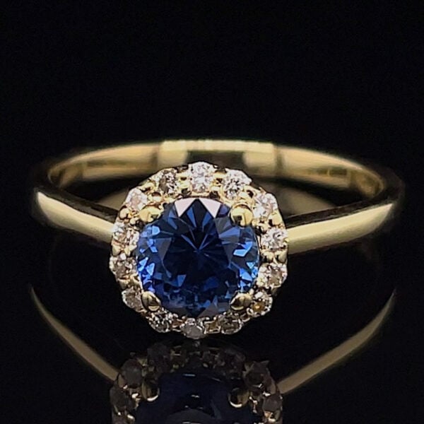 Gold ring with a deep blue oval-cut sapphire surrounded by a halo of diamonds on a dark background.