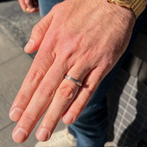 Close-up of a left hand with a simple silver wedding band on the ring finger, wearing a gold watch on the wrist.