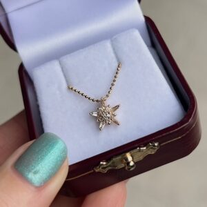 Gold-toned star pendant necklace with small stones displayed in a white padded jewelry box.