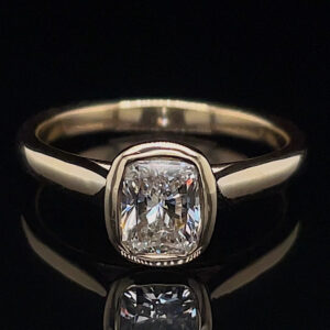 Silver band engagement ring with a cushion-cut diamond centerpiece on a dark, reflective surface.