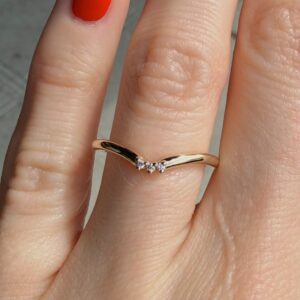 Close-up of a delicate gold ring with three small diamonds on a finger, with red nail polish nearby.