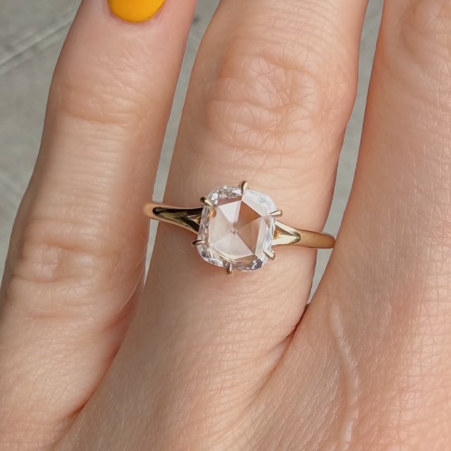 Close-up of a gold solitaire ring with a large clear gemstone on a finger.
