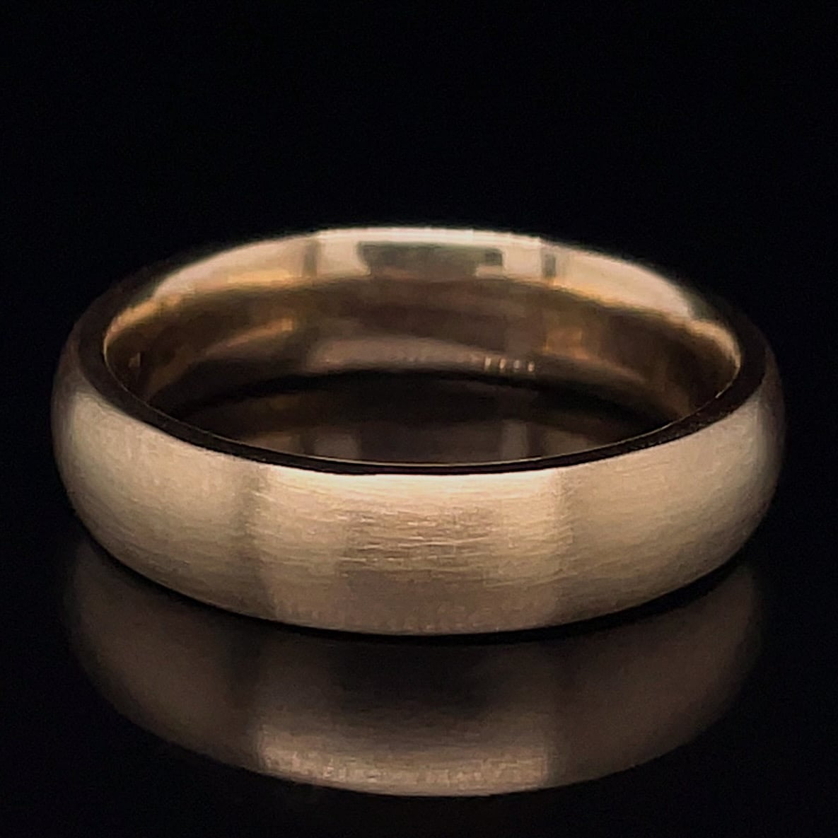 Brushed silver wedding band photographed on a black background, showing its simple, wide metal surface.
