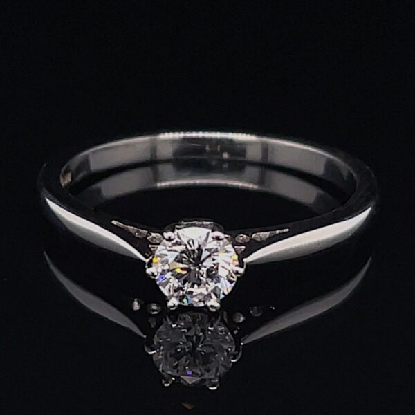 Engagement ring with a round-cut center diamond on a silver band against a black background, reflecting below it.