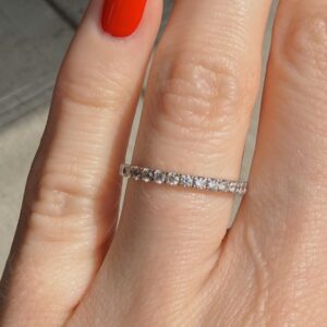Close-up of a diamond eternity ring on a finger with red nail polish.