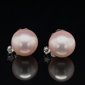 Pair of pink pearl stud earrings with diamond accents on a black reflective surface with subtle reflection.
