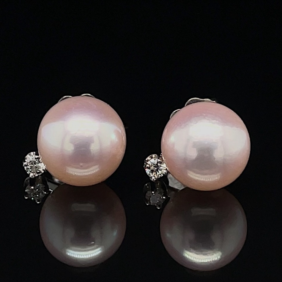 Pair of pink pearl stud earrings with diamond accents on a black reflective surface with subtle reflection.