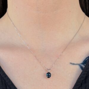 Silver chain necklace with a dark oval blue gemstone pendant resting on the neck.