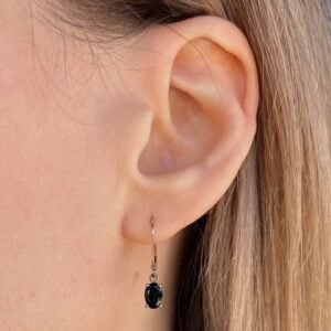 Close-up of a woman's ear wearing a gold hoop earring with a small black gemstone pendant.