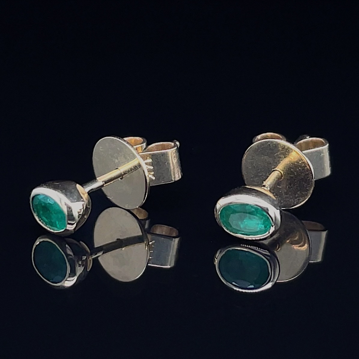 Silver cufflinks with oval emerald green stones on a black reflective surface, viewed from above.