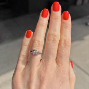 Close-up of a hand with bright red nails wearing a silver ring with a square diamond on the ring finger.