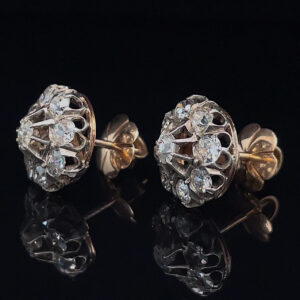 Pair of diamond cluster stud earrings set in gold on a black reflective surface, showing intricate lattice design and backings