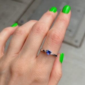 Close-up of a hand with bright green nails wearing a silver ring featuring a blue gemstone and small side stones on the ring finger.