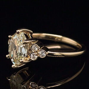 Gold engagement ring with a large cushion-cut center diamond and three small side diamonds on a black background.