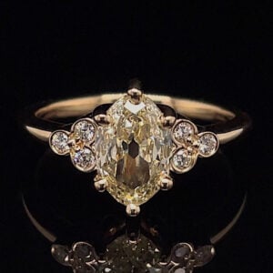 Engagement ring with a large oval yellow diamond center and small round diamonds along the sides on a gold band, against a black background.