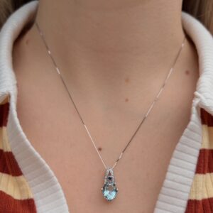 Silver necklace with a blue teardrop pendant on a person’s chest, with a striped shirt visible in the background.