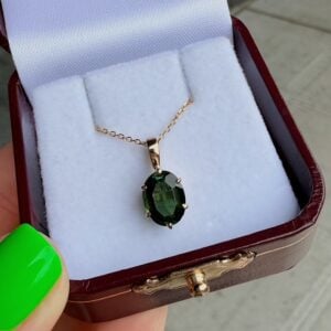 Gold chain necklace with an oval green gemstone pendant resting on a white cushioned display inside a burgundy jewelry box.