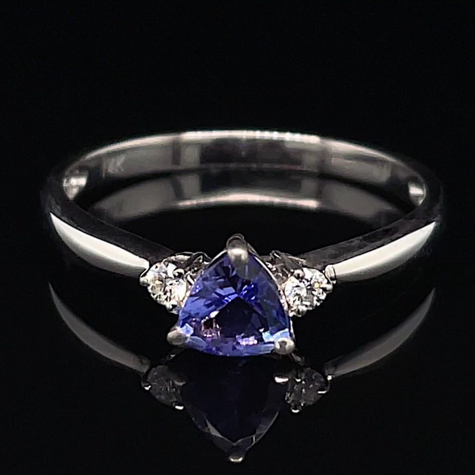 Silver ring with a pear-shaped blue-violet center stone flanked by two diamonds on a polished band against a black background.
