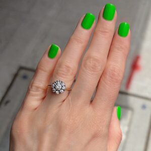 Woman's left hand with bright green manicured nails wearing a diamond cluster ring on the ring finger, close-up photo.]