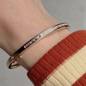 Gold bangle bracelet with a row of baguette-cut stones on a wrist wearing a red-and-cream striped sleeve.