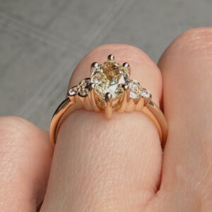 Close-up of a rose-gold ring with a large central oval diamond and smaller side stones on a finger crease, viewed from above