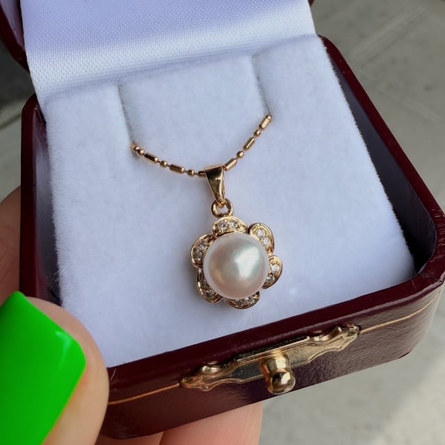 Gold flower pendant necklace with a pearl center and diamond accents, displayed in a white jewelry box