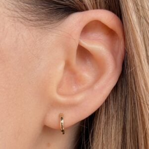 Close-up of a pierced ear wearing a small gold hoop earring on the earlobe.