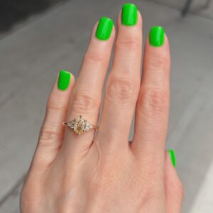 Hand with bright lime-green nails wearing a gold ring featuring a yellow center stone and small diamonds on the ring finger